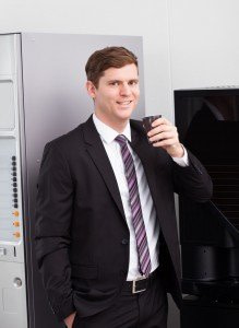 Image of business male in front of a vending machine with coffee held out in one hand